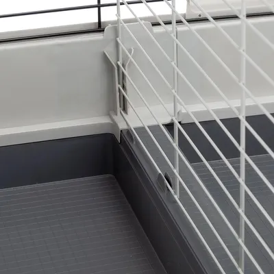 Vue rapprochée d’un coin de cage pour petits animaux, avec base en plastique gris et grille métallique blanche. Système d’attache visible entre la base et la grille.