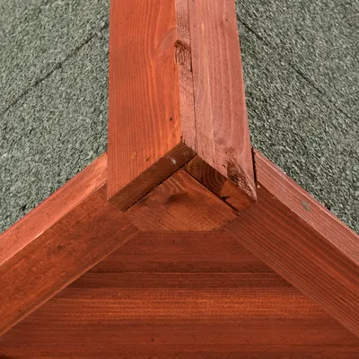 Detalle del tejado de una caseta para mascotas, con estructura de madera barnizada y cubierta de material asfáltico verde.