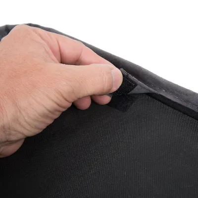 Close-up van een hand die een klittenbandsluiting op zwart textiel opent. Toont het eenvoudige gebruik van het product.