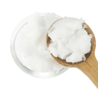 Masa blanca de aceite de coco en un cuenco de vidrio, parcialmente visible en una cuchara de madera.
