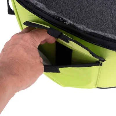 Main ouvrant une poche extérieure à scratch sur un sac vert en tissu, doublure intérieure grise visible. Fermeture éclair noire sur le dessus du sac.