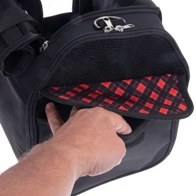 Sac noir avec poche avant ouverte, doublure intérieure à motif rouge et noir, main insérant un objet dans la poche. Fermeture éclair métallique visible en haut.
