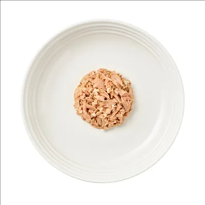 Nahaufnahme von zerkleinertem Thunfisch auf einem weissen Teller, präsentiert als Beispiel für die Konsistenz und Optik des Tierfutters.