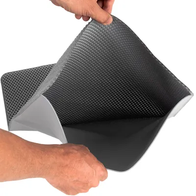 Grijze mat met antislipstructuur, wordt door een hand opgetild. Materiaal: kunststof met reliëf aan de boven- en onderzijde zichtbaar.