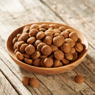 Croquettes rondes marron dans un bol en bois, posées sur une table en bois. Aucun emballage ni marque visible.