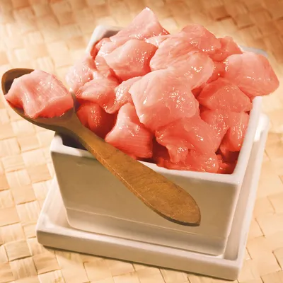 Bucăți de carne roz crudă într-un bol pătrat alb, cu lingură de lemn. Nu este vizibil niciun brand sau etichetă pe ambalaj.