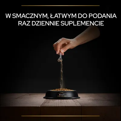 Ręka wsypuje proszek z miarki do miski z karmą Purina Pro Plan. Widoczny tekst: W smacznym, łatwym do podania raz dziennie suplemencie.