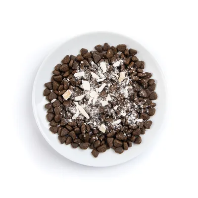 Bowl filled with dry pet food kibble topped with white powder and small chunks, showing product texture and appearance.