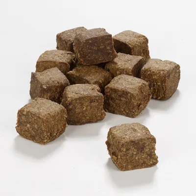 Morceaux cubiques de friandises brunes pour animaux, texture compacte et granuleuse, sans emballage ni marque visible, posés sur une surface blanche.