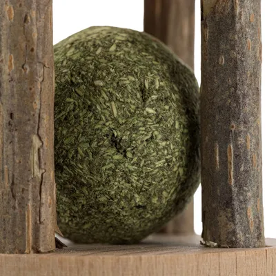 Bola de hierbas verdes prensadas, rodeada de palos de madera sobre una plataforma de madera.