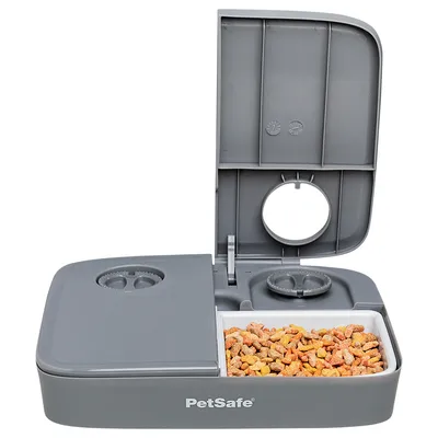 PetSafe Futterautomat mit grauem Gehäuse, geöffnetem Deckel und einer Schale mit Trockenfutter. Zwei Drehregler zur Einstellung sichtbar.