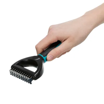 Hand holding a black grooming brush with blue handle and metal bristles, suitable for removing undercoat.