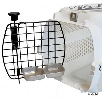 Transportín blanco con puerta metálica de rejilla abierta y dos comederos metálicos dobles sujetos a la puerta. Laterales con orificios de ventilación visibles.