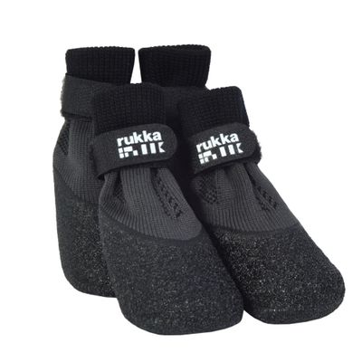 Vier graue Hundeschuhe mit schwarzem Klettverschluss und 'rukka'-Logo, auf einem moosbedeckten Steinboden platziert.