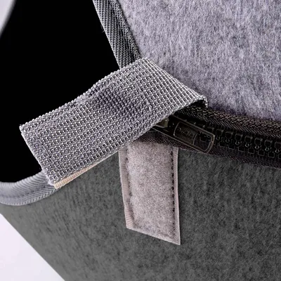 Close-up van grijs viltmateriaal met klittenbandsluiting en ritssluiting, toont de afwerking en functionaliteit van het product.
