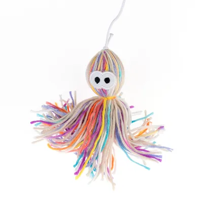 Juguete de hilos de lana de colores con bordado de ojos, colgando de un cordón blanco.