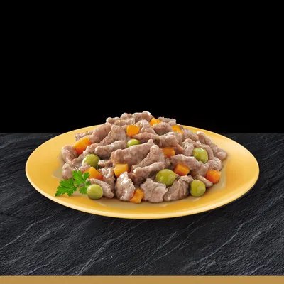 Gul tallerken med kødstykker, grønne ærter og orange gulerodsterninger i sovs, pyntet med et persilleblad.