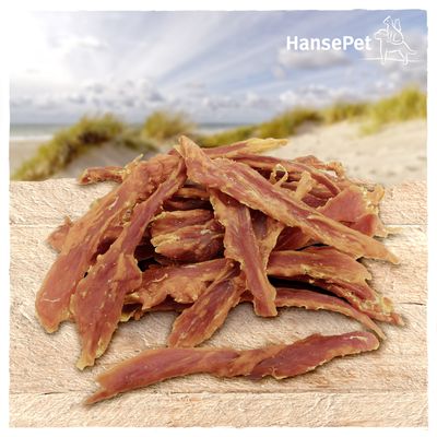 HansePet. Gedroogde vleesstrips op houten ondergrond, achtergrond met strand en duinen.