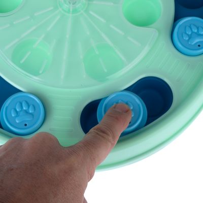 Interaktivt leksak med grön och blå yta. Ett finger trycker på blått element med tassmotiv för att visa funktionen.