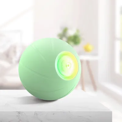 Balle verte en plastique avec un cercle lumineux jaune et vert sur le côté, posée sur une surface blanche. Aucun texte ou marque visible.