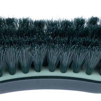 Близък план на четка с гъсти, тъмнозелени пластмасови влакна и извита пластмасова дръжка.