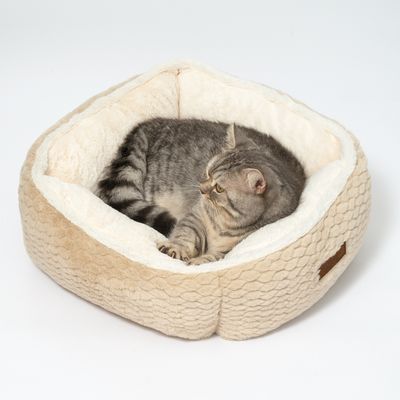 Kattbädd av beige tyg med mjuk, vit innervaddering. Grå katt ligger avslappnat i den.