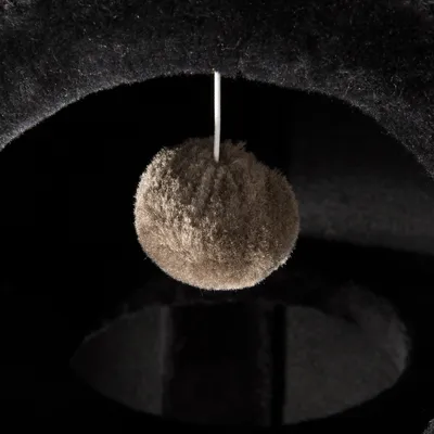 Hängande boll av mjukt tyg, fäst med snöre i ett mörkt klösträd för katter. Endast bollen och en del av klösträdet syns.