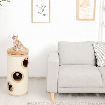 Cylindrical scratching post with multiple openings and padded lying surface next to a grey sofa. Red tabby tomcat sitting on top of the scratching post.