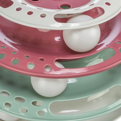 Jouet interactif en plastique à trois niveaux superposés de couleurs rose, blanc et vert, avec des balles blanches visibles dans chaque niveau.