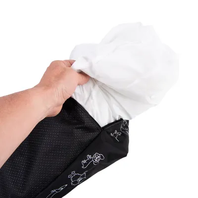 Main insérant un coussin blanc dans une housse noire à motifs de chiens dessinés en blanc, tissu visible avec texture perforée.