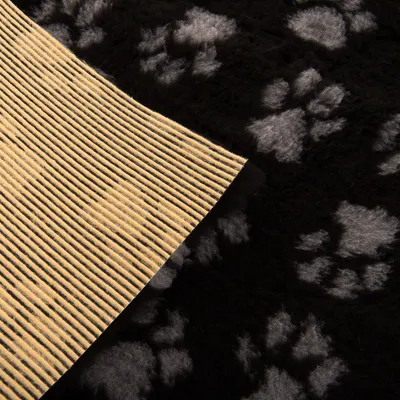 Nahaufnahme einer schwarzen Matte mit grauen Pfotenmustern und rutschfester Unterseite aus gelbem Gummi. Nahaufnahme einer schwarzen Matte mit grauen Pfotenmustern und rutschfester Unterseite aus gelbem Gummi.