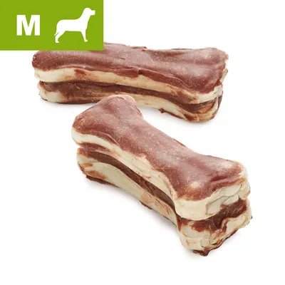 Two medium-sized bone-shaped chews with layered brown and beige appearance, green box in corner shows letter M and a dog silhouette indicating medium size.