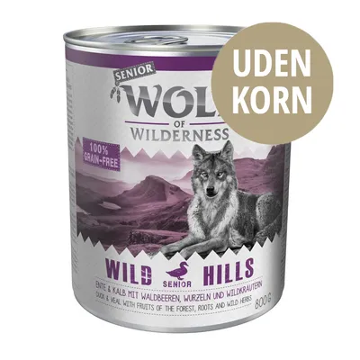 Wolf of Wilderness Senior Wild Hills dåse 800 g, tekst: UDEN KORN, 100% grain-free, and med and kalv mit Waldbeeren, Wurzeln und Wildkräutern. Billede af ulv foran bjerglandskab.
