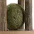 Green herb ball made of compressed material, surrounded by wooden sticks on a wooden platform.