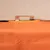 Detailansicht einer orangefarbenen Stofftasche mit Metallhalterung und Schrauben an einer Holzplatte befestigt.