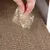 Hand sprinkles dried herbs from a plastic bag onto a brown corrugated cardboard surface.