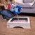Person pouring Sanicat litter from a bag into a rectangular tray, demonstrating how to fill the tray with litter.