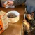 Person serving wet food from a pouch into a bowl on a kitchen counter, with a dog watching. Product box shows flavours: chicken with beef, duck, tuna, and salmon.