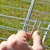 En hånd viser, hvordan metalclips fastgøres til et gitter for at sikre forbindelsen.
