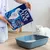 Ever Clean Extra Hygiene Katzenstreu wird in eine Katzentoilette gefüllt, weiße Katze daneben. Verpackung mit Produktinformationen sichtbar.