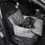 Dog sitting in a grey car seat dog bed with check pattern and safety belt. Bed placed on the front passenger seat of a car.