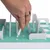 A hand shows a white stick being removed from a green interactive toy. Toy with obstacles and openings for activities.
