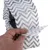 Hand showing the elastic structure and zigzag pattern of a grey disposable nappy with adhesive closure.