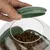 Hand opens green lid of a transparent container with brown dry food pieces.