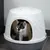 Chat noir et blanc visible à l’entrée d’une maison de toilette pour chat en plastique blanc et gris, forme arrondie avec ouverture frontale large.