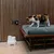 Il gatto è seduto su un cuscino, accanto a una fontanella bianca con la scritta CAT MATE sul pavimento davanti a un rivestimento in legno.