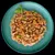 Chunks of wet pet food with visible peas and carrots served on a plate, showing texture and ingredients for product comparison.
