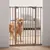 Barrière de sécurité en métal installée dans un encadrement de porte, chien de grande taille derrière la barrière, intérieur de maison visible en arrière-plan.