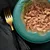 Chunks of meat in gravy served on a green plate with a sprig of rosemary, shown for product texture and appearance.