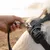 Hand attaches a lead with metal clip to a black dog harness with Ruffwear logo.